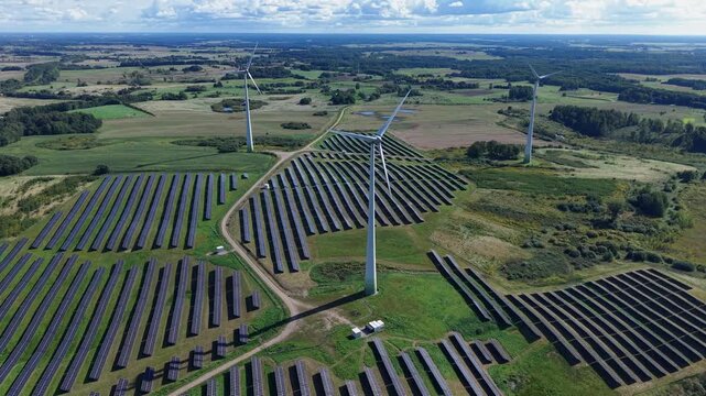 Drone video captures vast solar farms and towering wind turbines across rolling fields under a bright sky, showcasing green energy infrastructure from an aerial perspective.