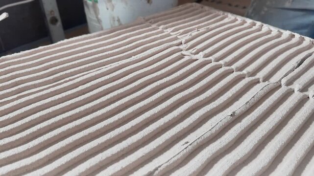 Close-up of evenly combed tile adhesive with parallel ridges, showing surface preparation for precise ceramic flooring during a professional indoor renovation.