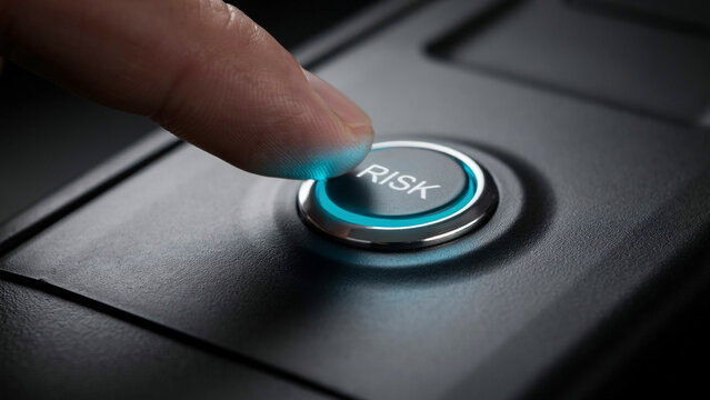 A human finger pressing a circular button with the word risk printed on it, glowing with a bright blue light in darkness