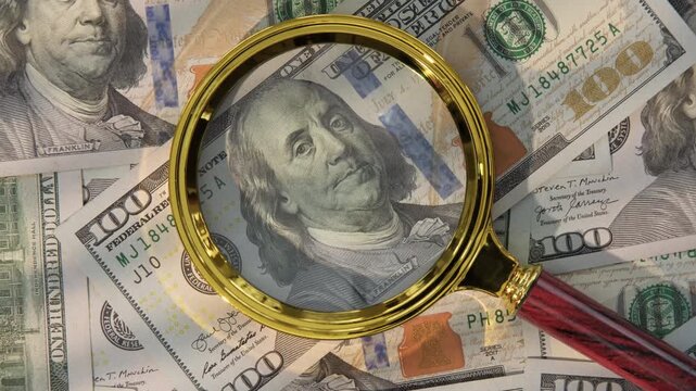 Magnifying glass on portrait of Benjamin Franklin on obverse of 100 dollar US bill against background of cash, identifying counterfeit, visual inspection