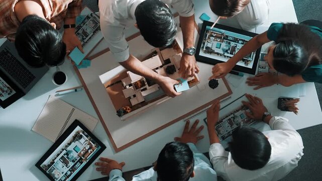 Top down view of manager pointing at house model and explain building design. Aerial view of architect engineer brainstorming about interior construction while tablet display house plan. Alimentation.