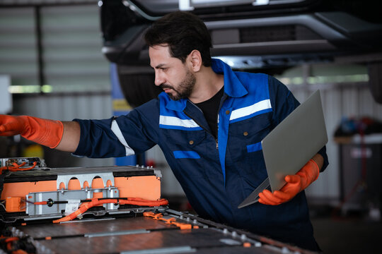 Electric vehicle technician performing battery repair in modern automotive shop with tools and equipment