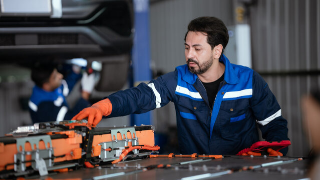 Technicians discussing electric vehicle battery repair in a modern workshop with advanced diagnostic equipment