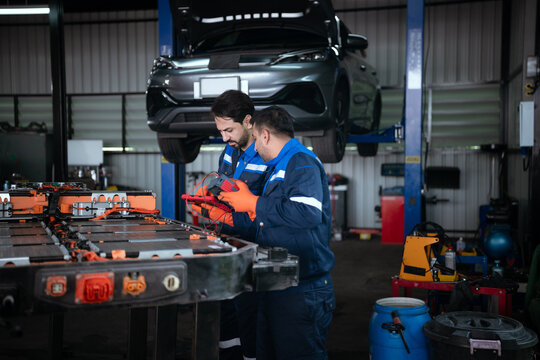 Two technicians are inspecting an electric vehicle battery in a repair shop.
