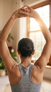 Athletic woman stretching arms and back near bright room window