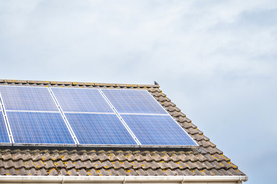 Wide composition of photovoltaic panels mounted on a tiled house roof with a large expanse of pale sky with copy space, alternative energy.