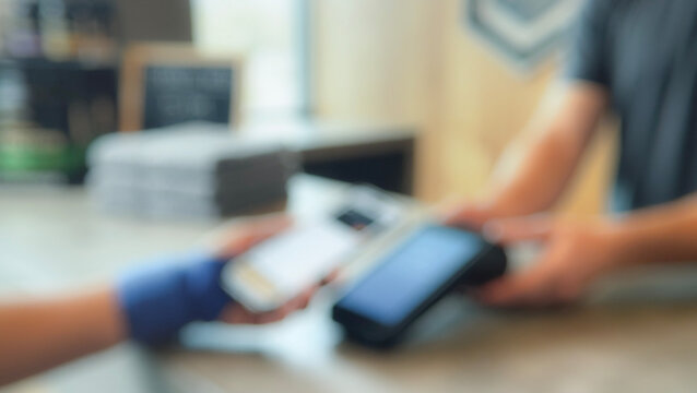 A blurred scene of a customer making a mobile payment at a retail counter with a card reader and a smartphone being exchanged.