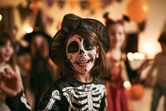Skeleton at Halloween Costume Party Smiling Girl Wearing Witch Hat and Skull Makeup Among Festive Guests