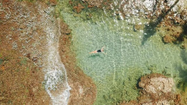 Woman floating in clear Costa Rica natural tide pool surrounded by reef in sunlight