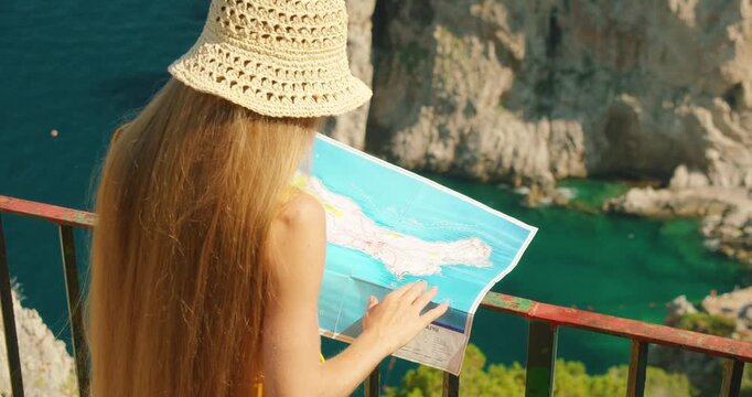 Woman reads island map above vivid turquoise bay and Faraglioni sea stacks in Capri, Italy