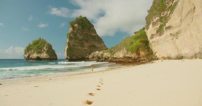Woman explore sandy shore of Diamond Beach with turquoise ocean water and towering rocky cliffs in Nusa Penida Bali