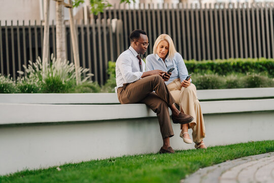 Diverse business people collaborating using smartphones outdoors