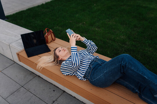 Woman relaxing on park bench checking smartphone