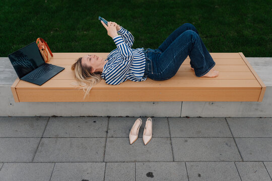 Woman relaxing outdoors with smartphone and laptop