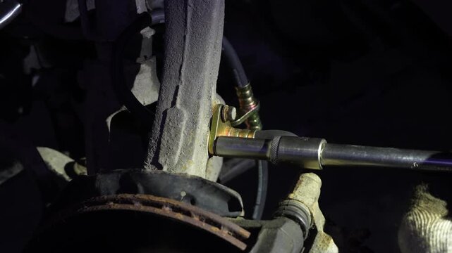 Mechanic uses a socket wrench to bolt brake hose bracket.