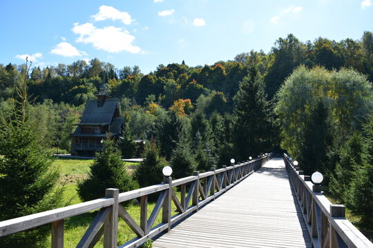 Bridge leading to a wooden house surrounded by trees and a bright sky