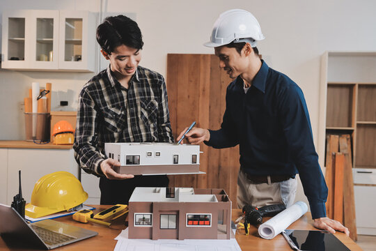 Asian architect and engineer team checking architectural house model using measuring tape on the table at office studio.