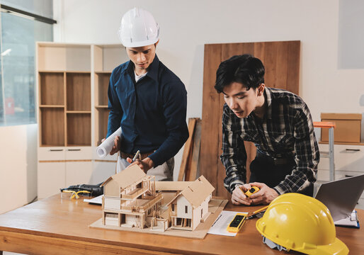 Asian architect and engineer team checking architectural house model using measuring tape on the table at office studio.