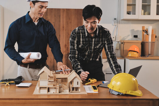 Asian architect and engineer team checking architectural house model using measuring tape on the table at office studio.