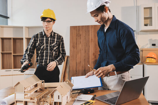 Asian architect and engineer team checking architectural house model using measuring tape on the table at office studio.