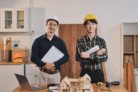 Asian architect and engineer team checking architectural house model using measuring tape on the table at office studio.