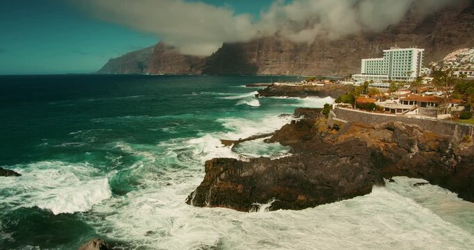 Powerful sea waves crash on rocky shore, stormy ocean with natural swimming pool in Tenerife Canary Islands. Charco de Isla Cangrejo. Water foam splashing on cliffs in slow-motion.