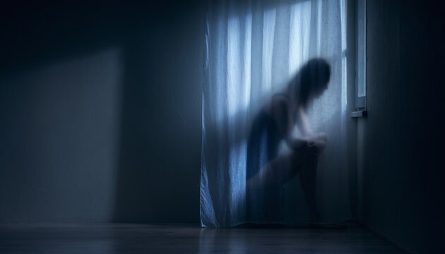 Blurred silhouette of a lonely person standing behind a sheer curtain in a dark room reflecting anxiety and isolation