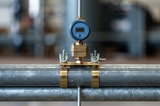 A digital pressure gauge is clamped onto a metal industrial pipe in a workshop setting.