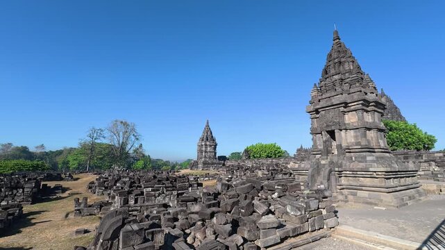 Historic Prambanan shrine rises above extensive stone ruins beneath vivid blue skies in the ancient Hindu temple complex.