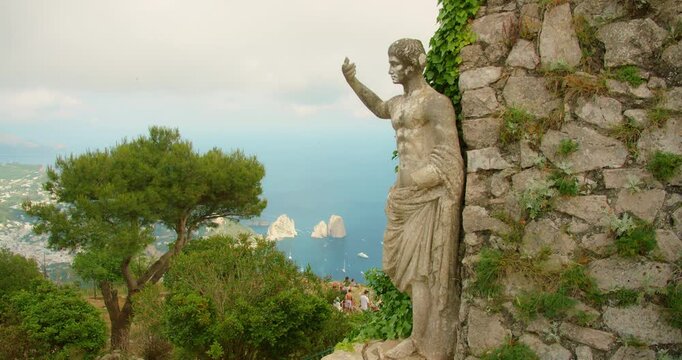Ancient Statue of Emperor Augustus above lush trees with Faraglioni sea stacks and Capri island view from Monte Solaro
