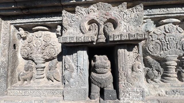 Ancient stone relief panels display carved guardian figures and mythological ornamentation on the walls of Prambanan Temple.