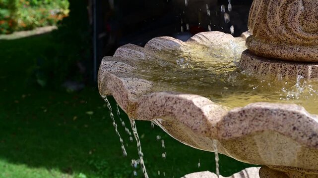 Water flowing and splashing over the rim of an ornamental stone garden fountain in slow motion