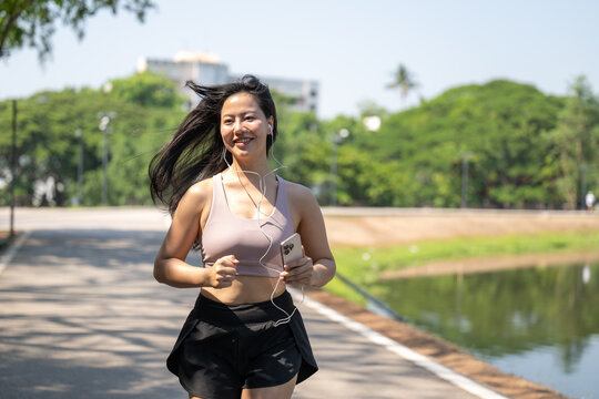 Woman Jogging Outdoors Along Park Pathway With Nature Scenery and Body Fitness in Bright Sunshine