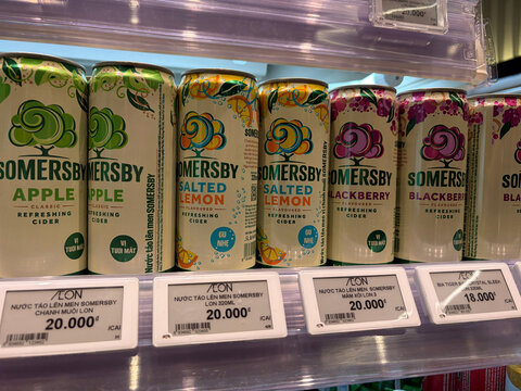 A display of flavored cider cans arranged on a shelf. The cans are labeled with different fruit flavors, including apple, lemon, and blackberry. They feature colorful designs.