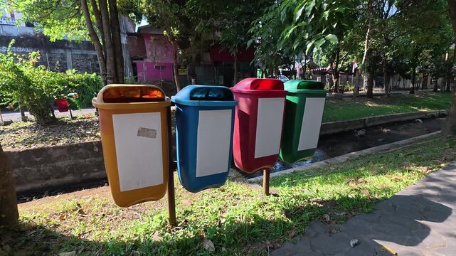 Colorful recycling bins beside a sunny green park walkway