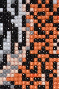A top down close up view of a partially completed diamond painting section showing rows of round black, orange, brown, and grey resin rhinestones placed on a sticky canvas grid