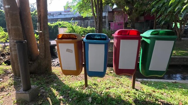 Four colorful waste sorting bins standing beside park greenery