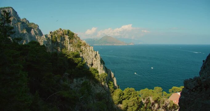 Rocky green coastline of Capri island with distant Sorrento peninsula on summer day