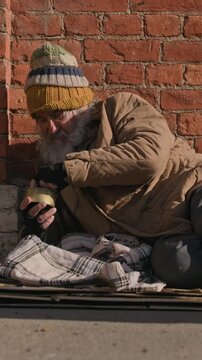Vertical shot of senior Caucasian homeless man receiving charity donation in tin can on city sidewalk. Clip suitable for social welfare documentaries and NGO fundraising campaigns