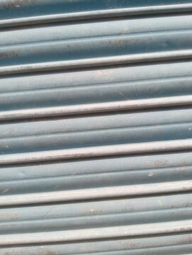 Blue metal roller shutter texture. Horizontal parallel slats and panels with weathered surface. Industrial background and security door abstract pattern for architectural design photography.