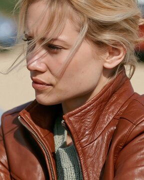 Blonde woman in brown leather jacket gazes thoughtfully