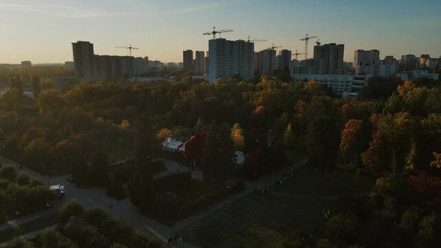 Drone view over autumn park and construction cranes on city skyline in Kyiv