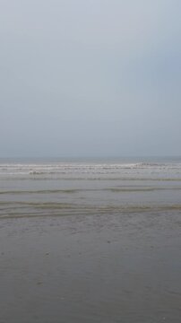 Calm ocean waves washing over a sandy beach on a foggy, overcast day. Serene and tranquil seascape background.