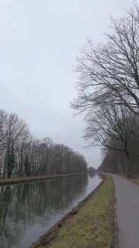 Serene POV walking shot along a canal towpath with bare winter trees on an overcast day.