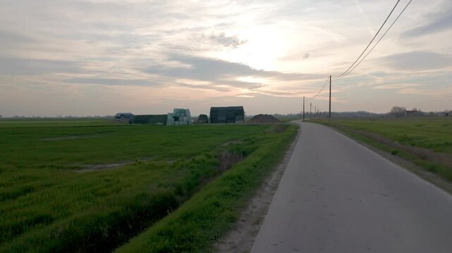 POV journey on an empty asphalt road through green fields in the rural landscape at dusk.