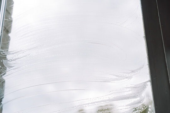 Curved cleaning foam streaks across a window without hands against a cloudy sky.