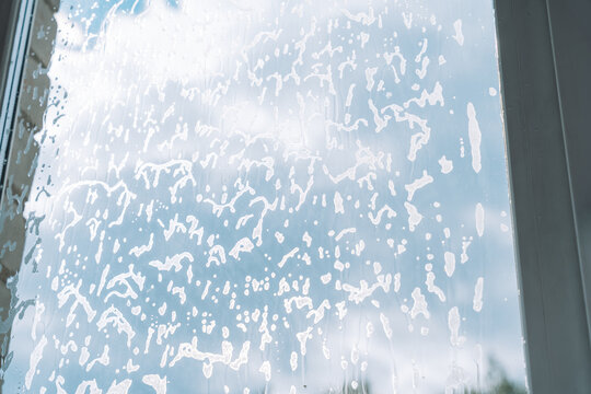 Dense cleaning foam scattered over a window against the sky with white window frames.