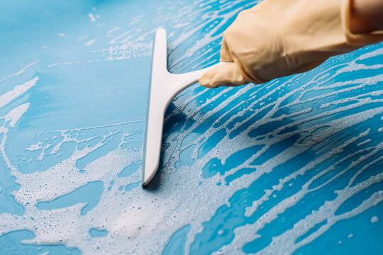 Gloved hand holding a squeegee upright on a foamy blue surface in close view.