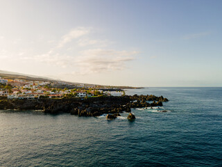 Coastal town strung along a black volcanic shoreline. Wide drone view of low white houses following a black volcanic shoreline on the western coast of Tenerife.  © Oksana