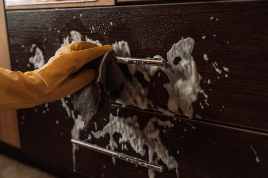 Gloved hand wiping foam beside a drawer handle with a gray cloth.